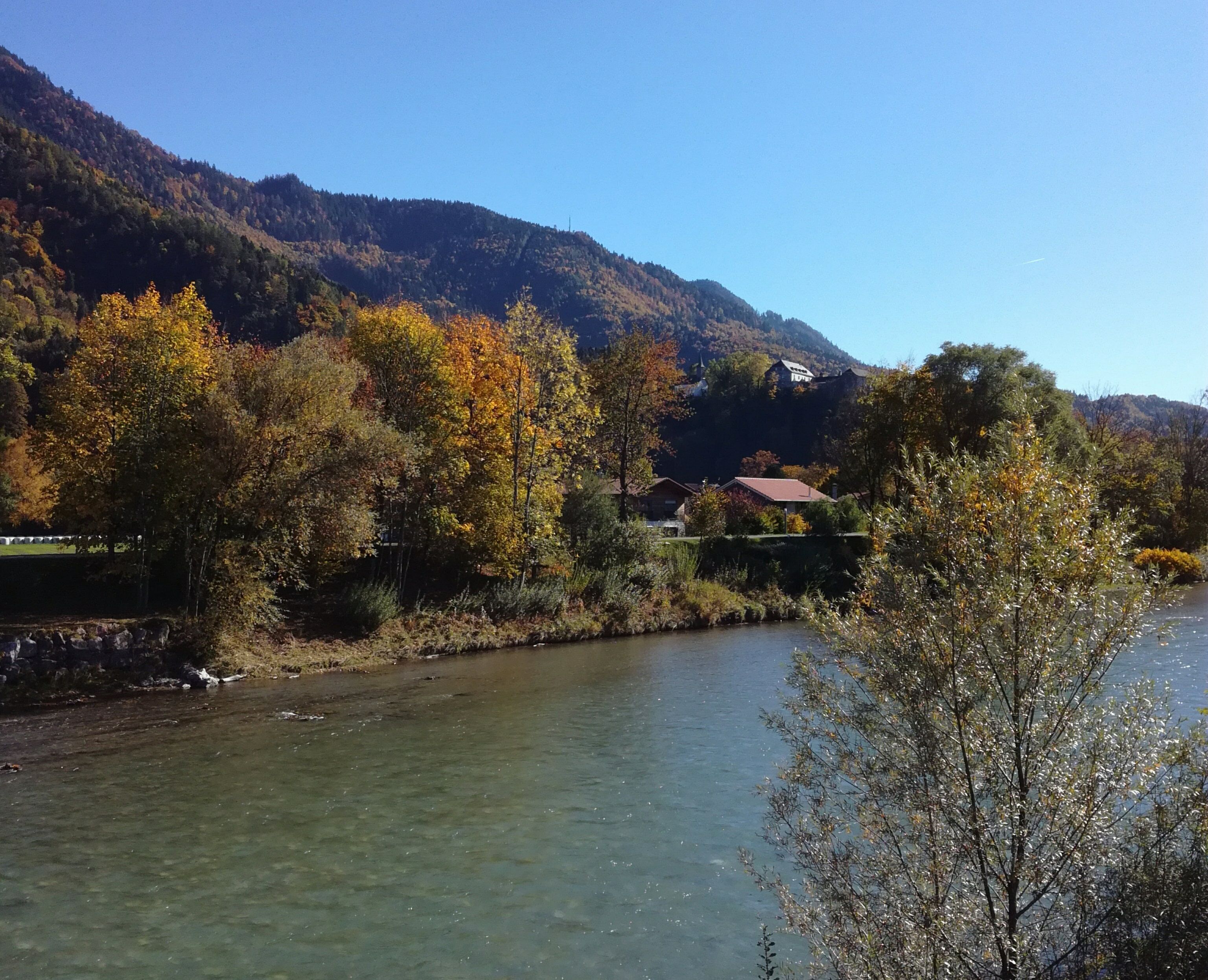 Ein Fluss mit klarem Wasser, umgeben von herbstlich gefärbten Bäumen und einem Berg im Hintergrund.