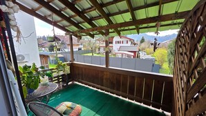 Un patio techado con césped artificial verde, una mesa de metal y una silla acolchada.