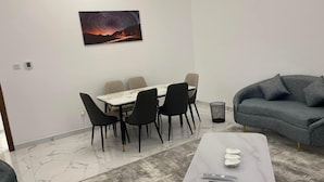 Un salon moderne comprenant un coin repas, un canapé gris et une table en marbre.