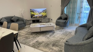 Un salon moderne doté d’un téléviseur à écran plat, de canapés gris, d’une table basse en marbre et d’un coin repas avec une table et des chaises blanches.