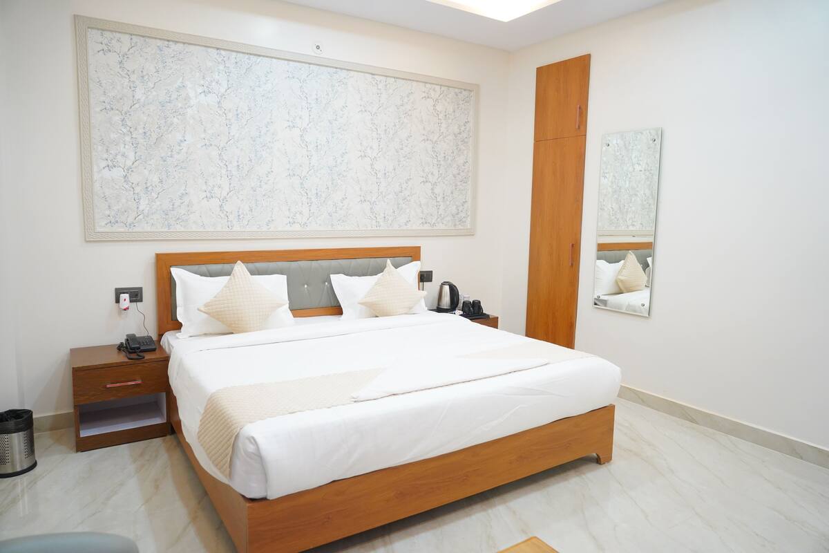 A neatly arranged bedroom with a large bed, a nightstand, a trash can, and a wall-mounted mirror.