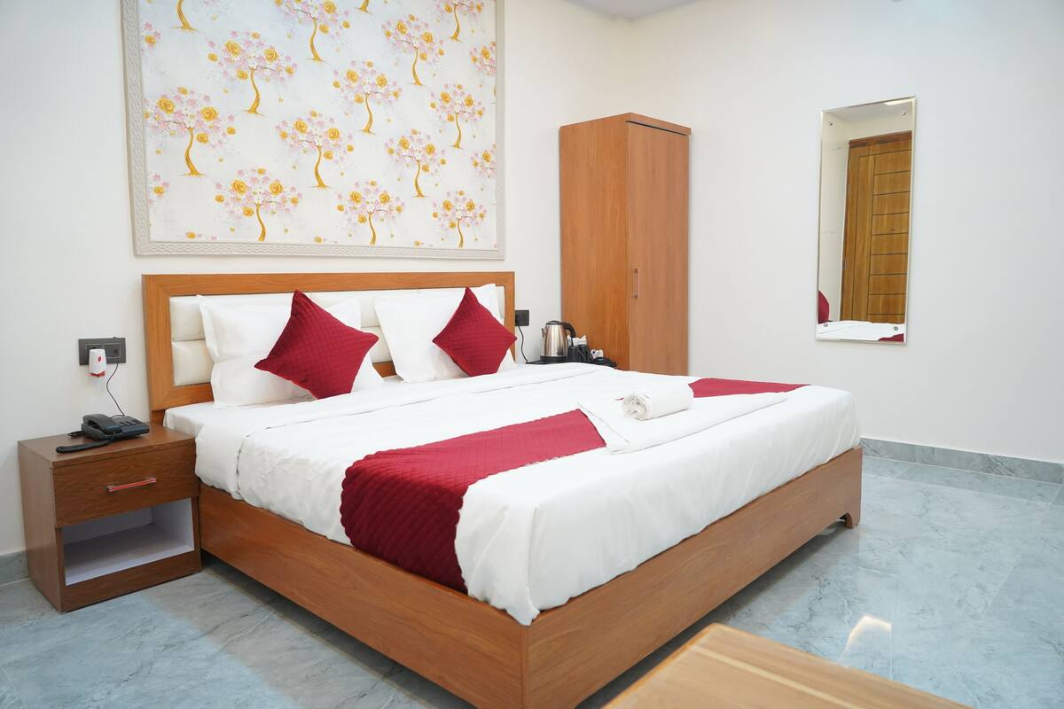 A neatly made bed with red and white bedding, a wooden nightstand with a phone, a wardrobe, and a painting on the wall.