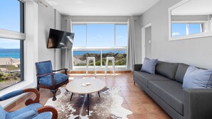 Un salon moderne avec une grande fenêtre, un téléviseur à écran plat, un canapé gris et un fauteuil bleu.