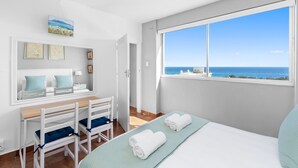 Une chambre avec un lit, un bureau, deux chaises et une vue sur la mer.