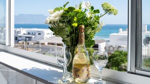 Une bouteille de vin de Durbanville Hills et deux verres posés sur un rebord de fenêtre, avec vue sur la mer et les bâtiments.