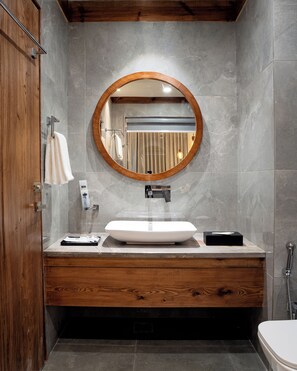 A modern bathroom with a wooden vanity, a round mirror, and a white sink. - The Highland Ladakh (Leh)