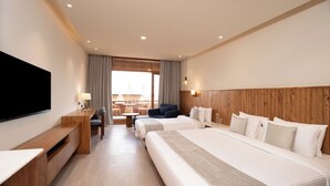 Habitación de hotel con dos camas, televisión, escritorio y balcón con vistas.