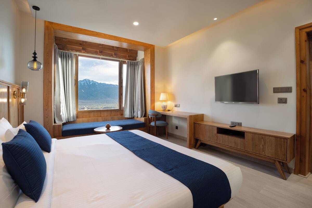 A hotel room with a large bed, a desk, a TV, and a view of the mountains.