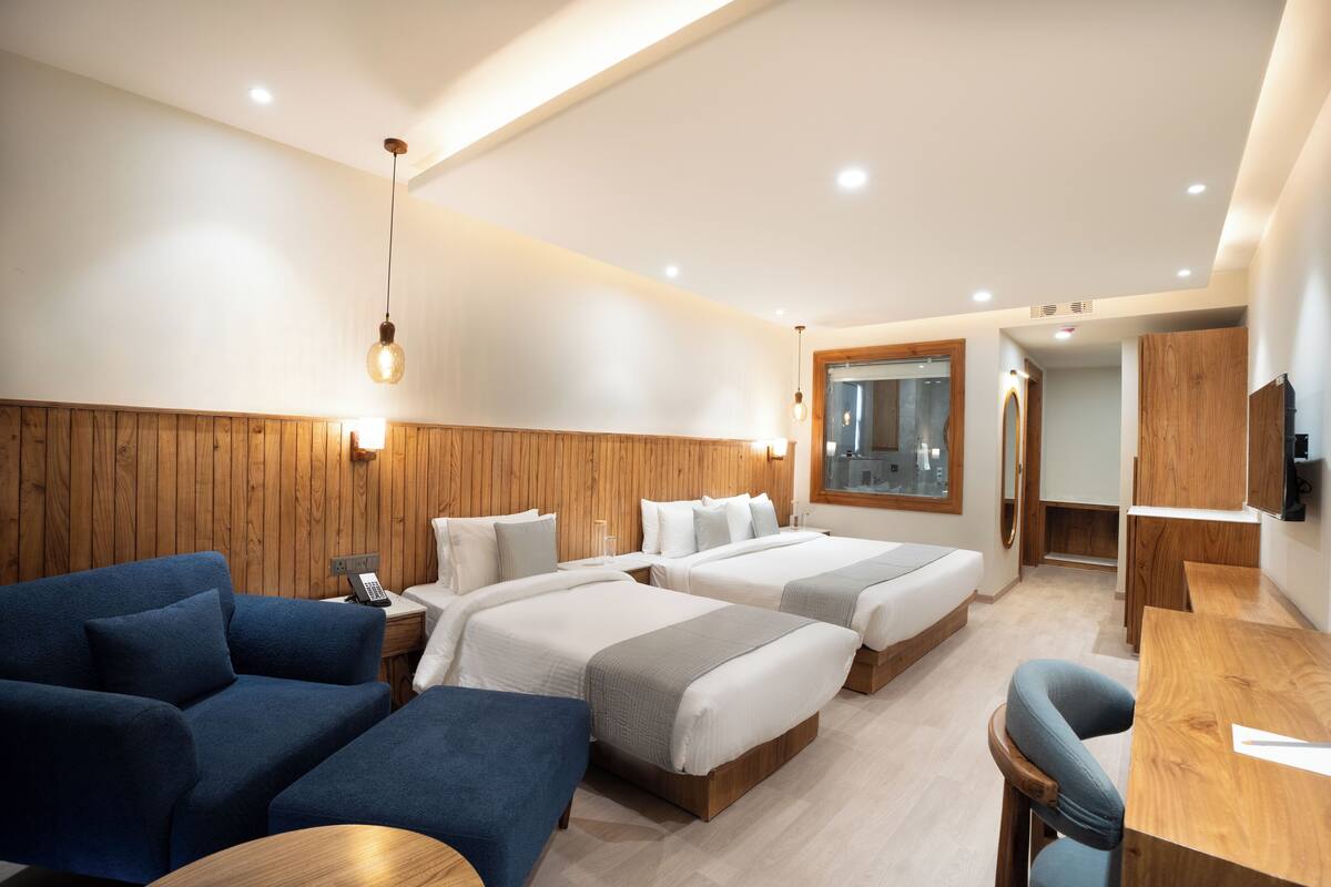 A hotel room with two beds, a sofa, a desk, and a mirror.