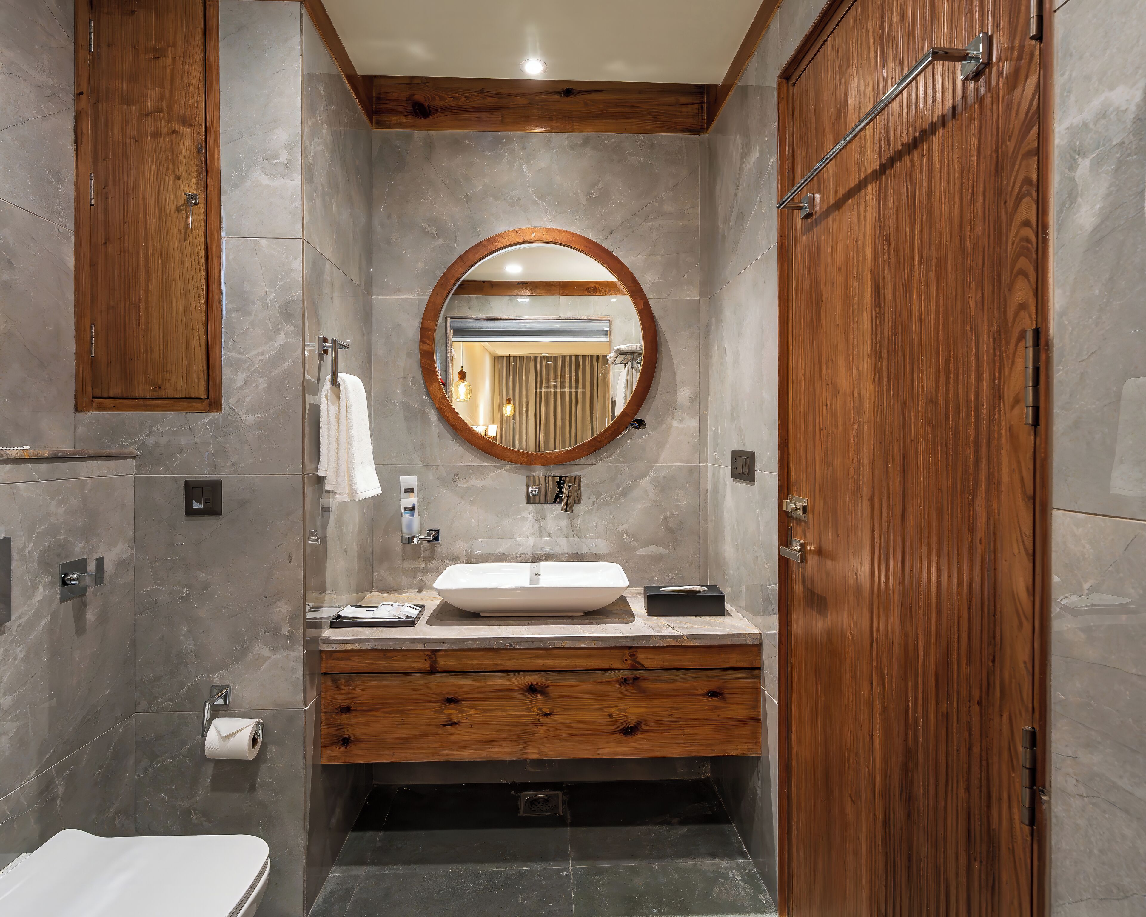Een moderne badkamer met een houten wastafelmeubel, een ronde spiegel en een ingebouwd toilet.