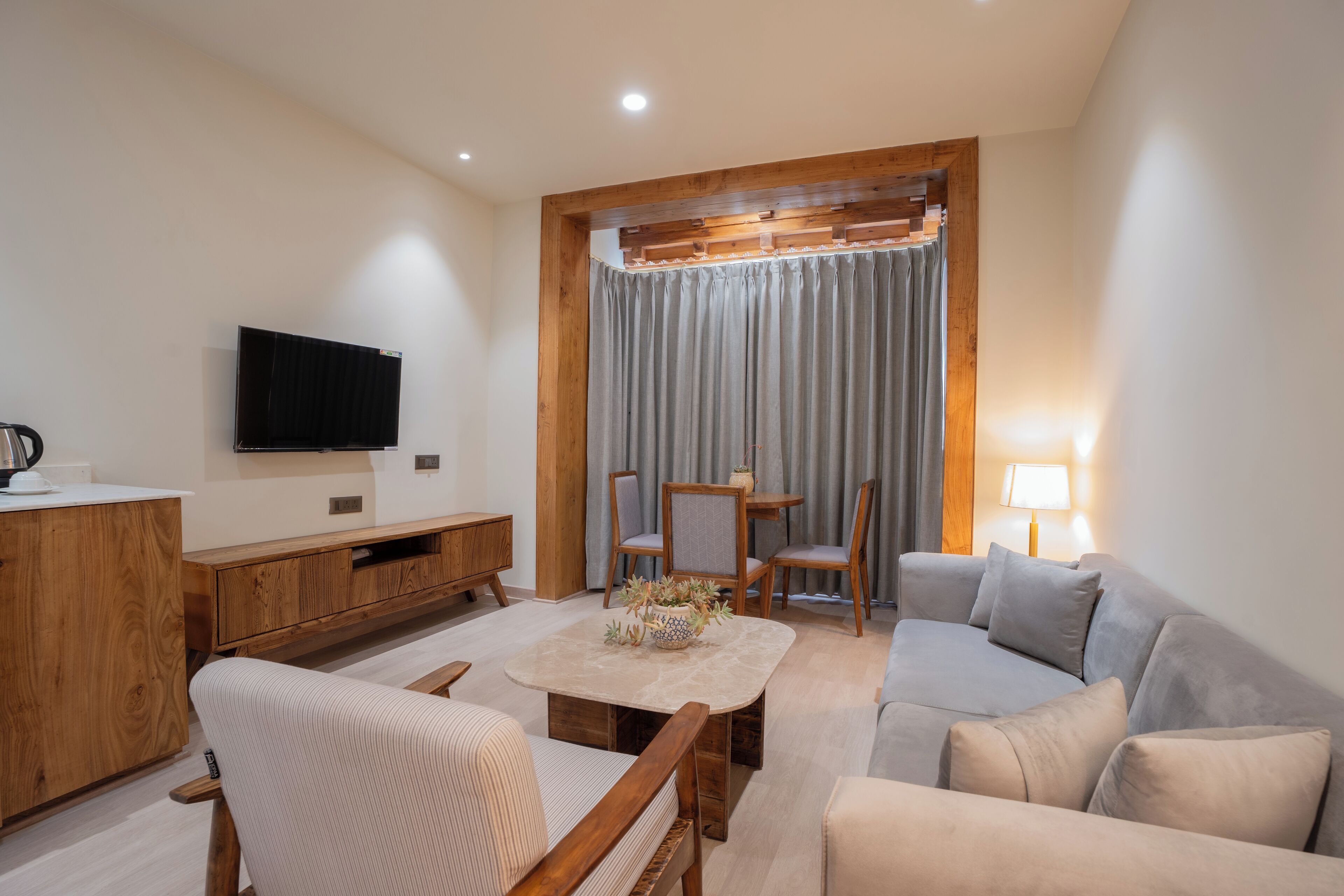 A modern living room with a wooden cabinet, a flat-screen TV, a grey sofa, a beige sofa, and a dining table with chairs.