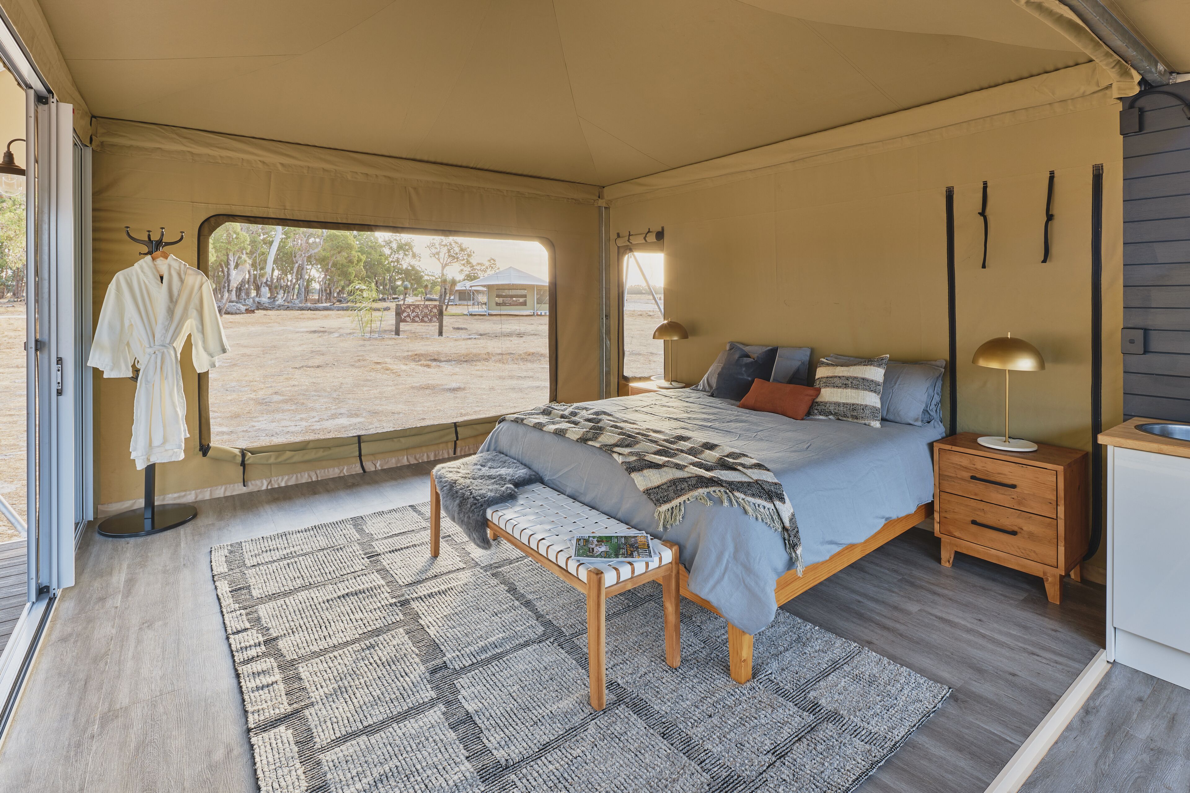 A spacious tented room with a large bed, a bench with a magazine, and a small table.