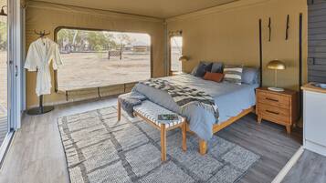 A spacious tented room with a large bed, a bench with a magazine, and a small table.