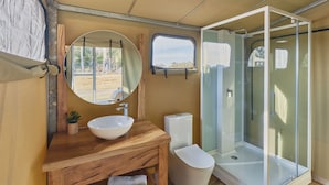 Une petite salle de bain avec un meuble-lavabo en bois, un miroir rond, un lavabo, des toilettes et une douche à parois de verre.