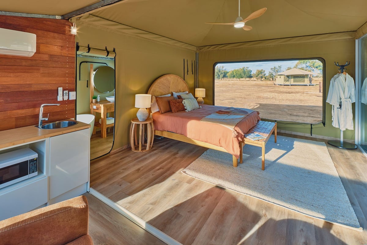 Een ruime slaapkamer met een bed, nachtkastjes, een klein bureau en uitzicht op het groen.