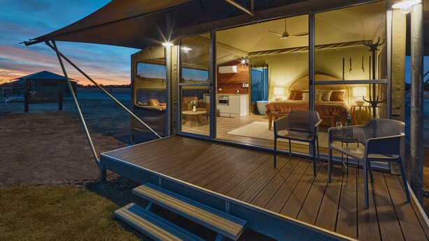 Un espace de vie moderne à aire ouverte, doté d’une terrasse en bois, de grandes fenêtres et d’un coin repas avec des chaises en métal.
