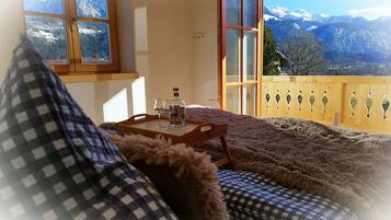 Ein gemütliches Zimmer mit einem karierten Sofa, einem Holztisch mit Flasche und Gläsern sowie Blick auf verschneite Berge durch große Fenster.