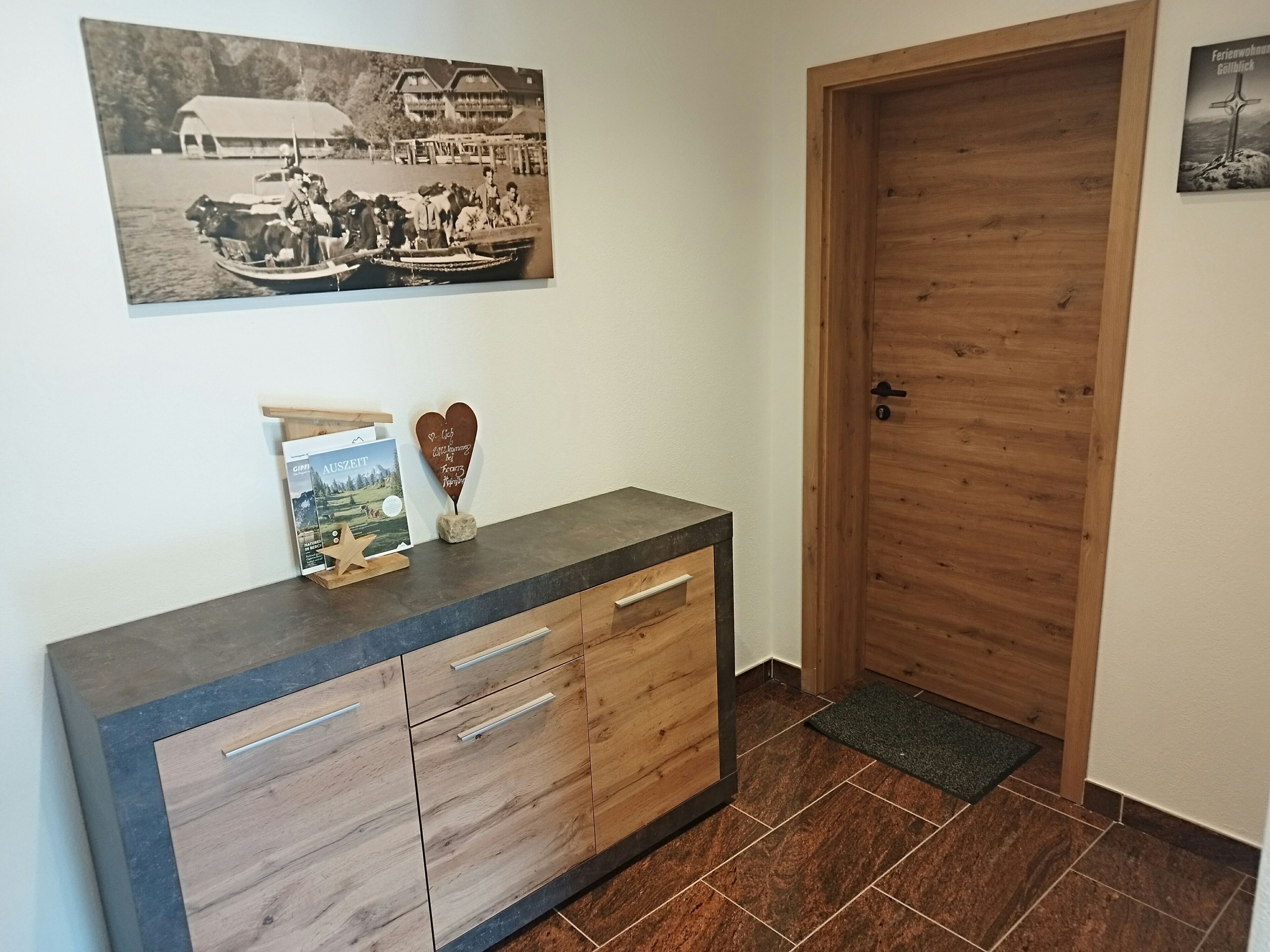 Una puerta de madera, un mostrador oscuro con cajones, una foto enmarco y una pequeña decoración con forma de corazón.