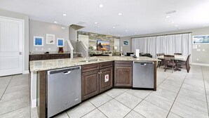 A modern kitchen with a large island, built-in dishwasher, and a dining area with a table and chairs. - Disney-Area Home w/ Themed & Media Room, Pool Table & Waterpark - 240CL (Kissimmee)