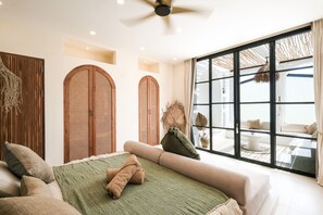 A modern bedroom with a large bed, a sofa, and a view of the outdoors through a sliding glass door. - Villa Coconut (Canggu)