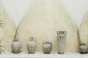 A row of five rustic ceramic vases of varying sizes against a textured wall, with a plant to the left. - Villa Coconut (Canggu)