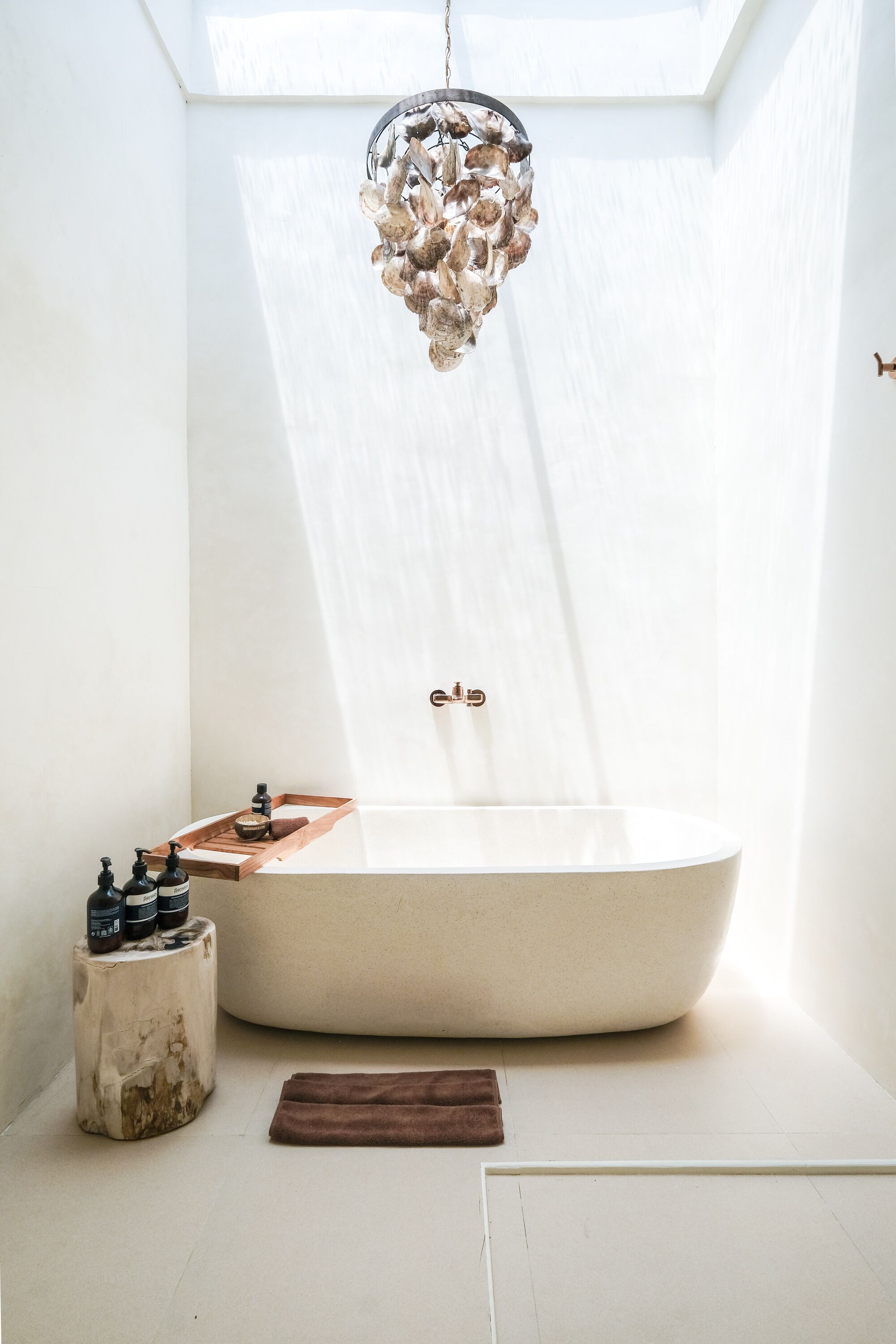 A modern bathroom with a freestanding bathtub, a wooden tray, and a decorative chandelier.