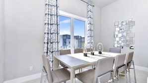 A modern dining area with a large table, four chairs, and a view of buildings through the window.