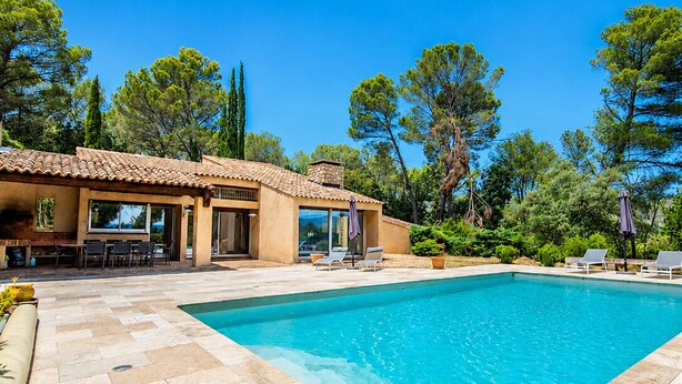 A swimming pool with a tiled deck, a patio area with seating, and a building with a tiled roof. - Villa San Michele - 70's Experience (Salernes)