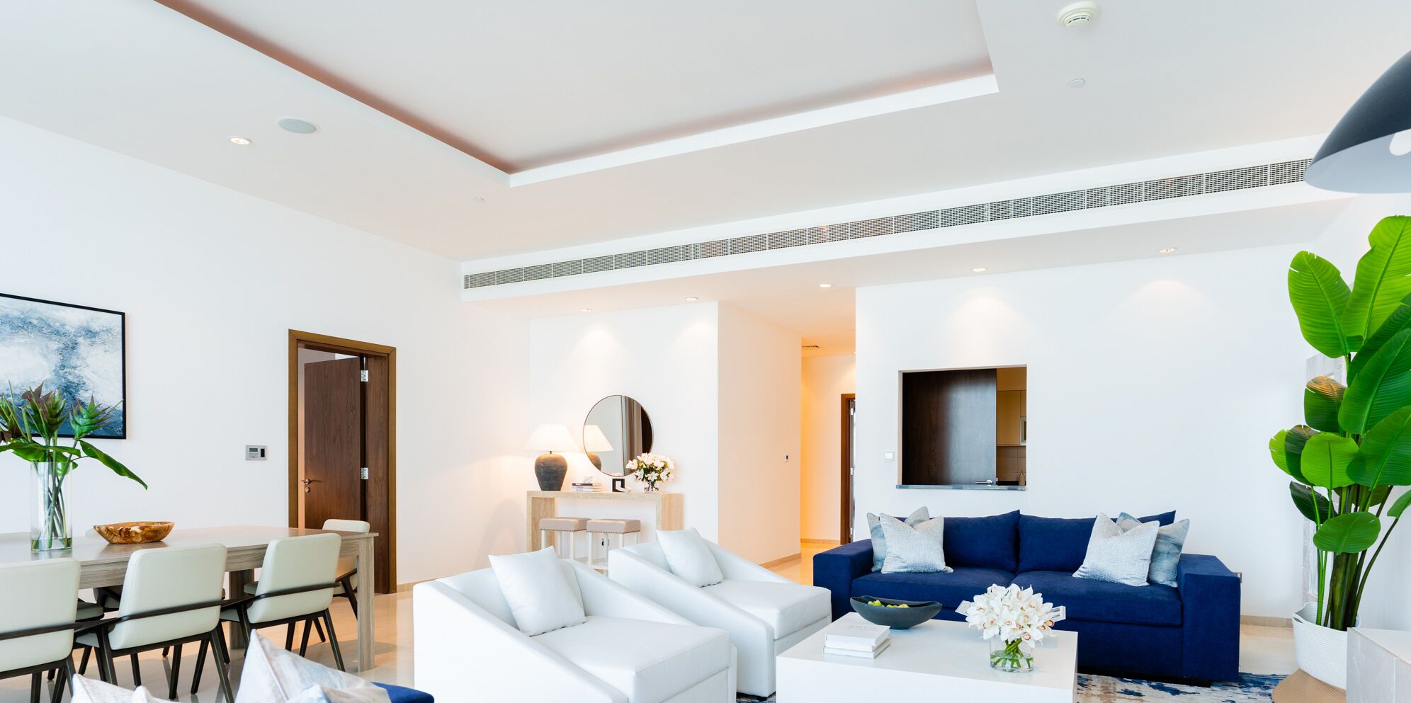 Una sala de estar moderna con un sofá blanco, un sofá azul y una mesa de centro. Hay una zona de comedor con una mesa y sillas.