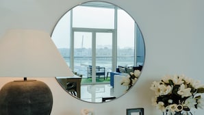 Ein runder Spiegel, der einen Blick auf einen Balkon mit Geländer, einem Stuhl, eine Lampe, eine Vase mit Blumen und eine Stapel Bücher zeigt.