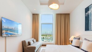 Ein Hotelzimmer mit einem großen Bett, einer Couch, einem Fernseher und Blick auf eine Marina durch ein großes Fenster.