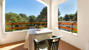 Un balcon avec une table et des chaises, donnant sur un paysage pittoresque avec des arbres et un ciel dégagé.