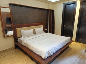 A single bed with a wooden headboard and white bedding in a room with wooden flooring and a dark door.