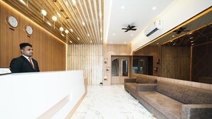 A hotel reception area with a wooden reception desk, a sofa, and a ceiling fan. - Madhav Residency Hotel & Banquet, Kalyan, Mumbai (Thane)