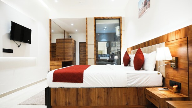 A modern hotel bedroom with a wooden headboard, a flat-screen TV mounted on the wall, and a large mirror reflecting the room. - Madhav Residency Hotel & Banquet, Kalyan, Mumbai (Thane)