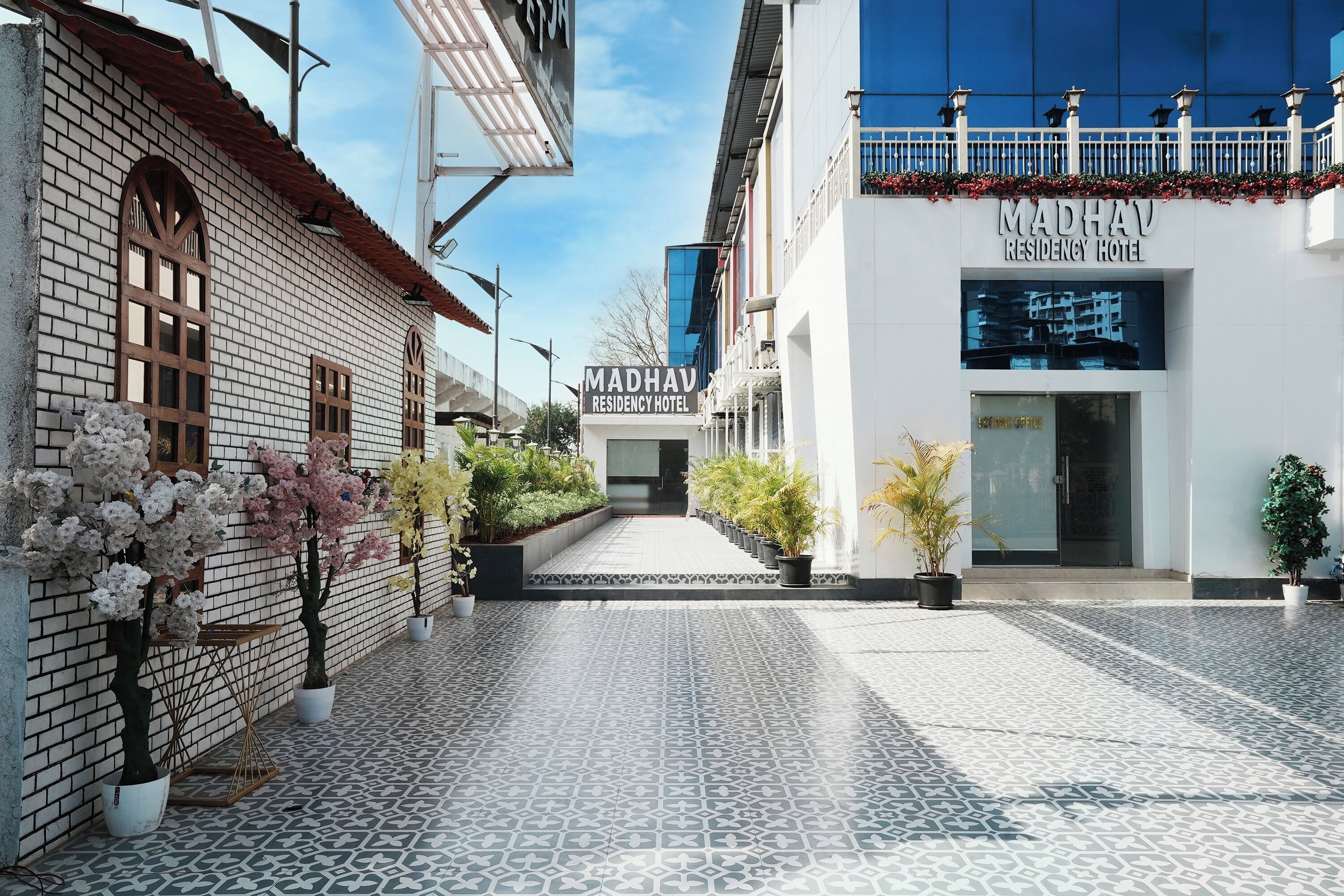 A hotel entrance with a tiled pathway, potted plants, and a clear sky.