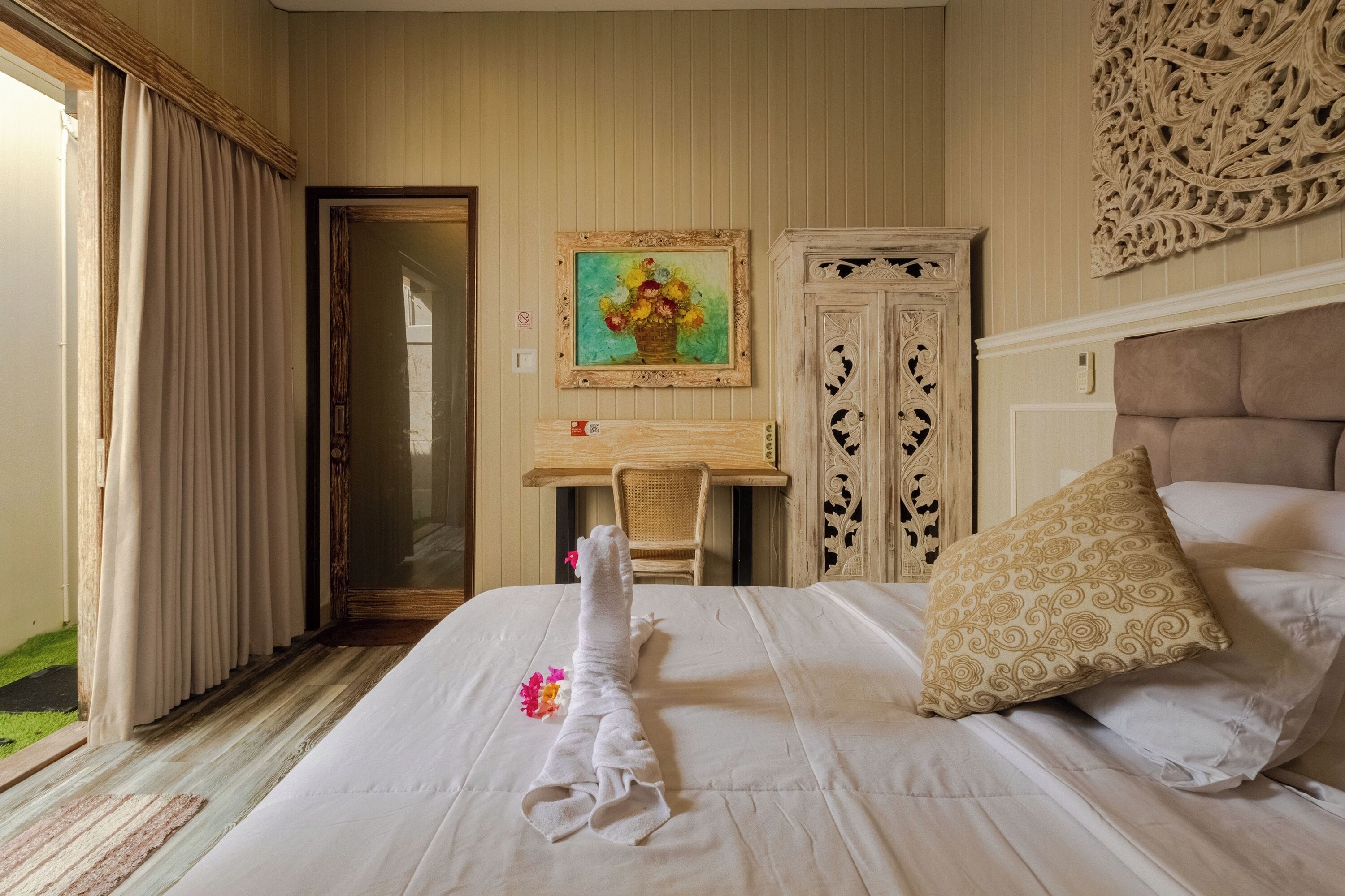 A hotel room with a bed, a chair, a desk, and a painting on the wall.
