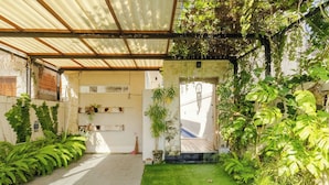 A covered patio area with artificial grass, potted plants, and a dreamcatcher decoration. - Rustic Pandawa Villa (Kutuh)