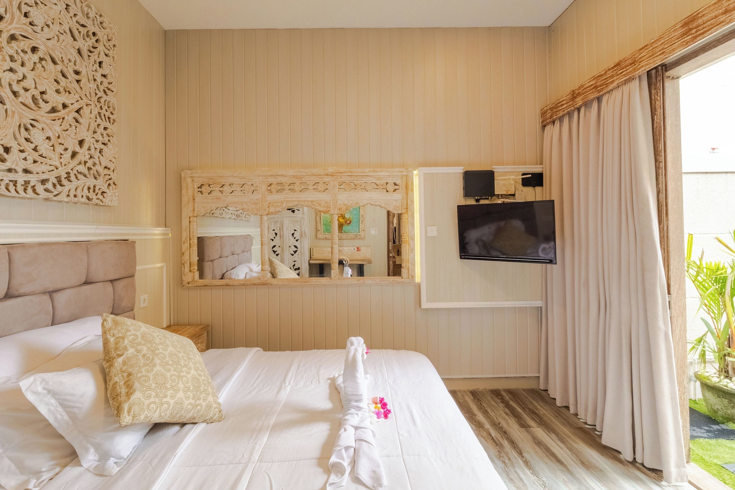 A hotel room with a large bed, a television, a mirror, and a window with curtains.