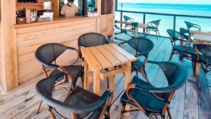 Un patio in legno con sedie e tavoli in vimini, un'area bar con scaffali e vista sull'oceano.