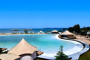 Un complexe hôtelier doté d’une grande piscine, de cabanes de plage et offrant une vue sur la mer.