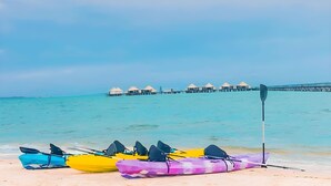 Kayak in fila su una spiaggia, con un molo e bungalow sull'acqua sullo sfondo.