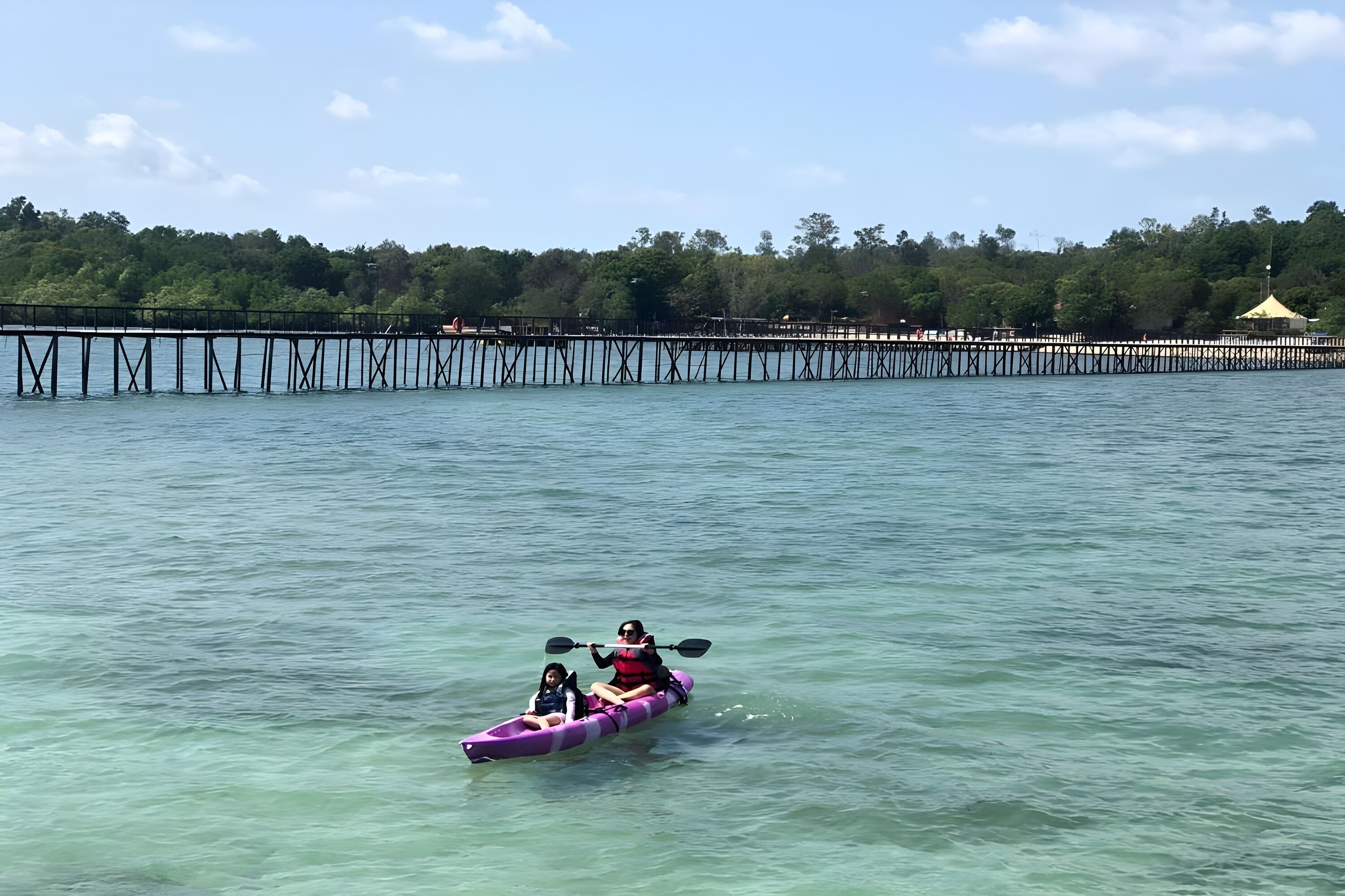 A kayak on calm water with a pier and trees in the background.