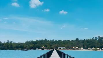 A wooden pier extending into a clear blue sea with a forested island in the background.