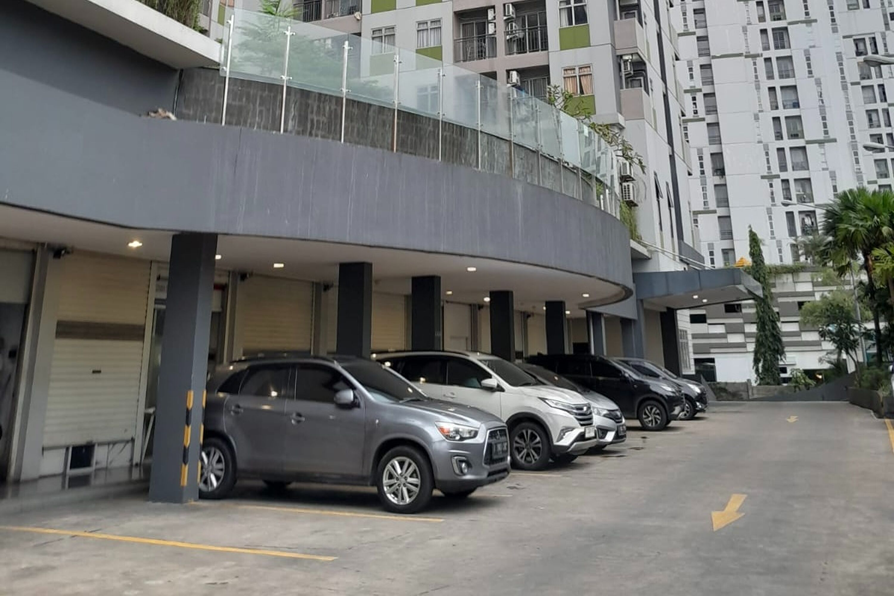 Un espace de stationnement où plusieurs voitures sont garées devant un immeuble à la façade incurvée et doté de balcons.