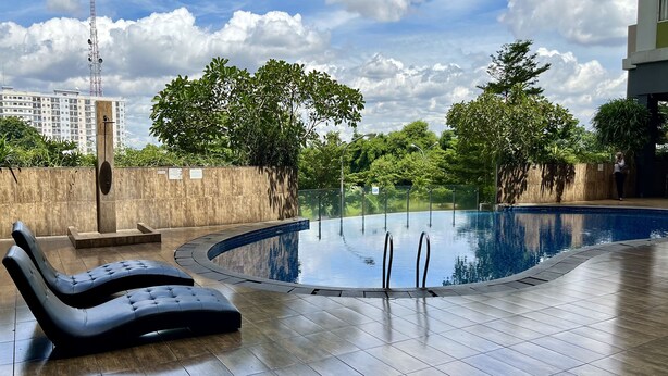 A swimming pool with lounge chairs, surrounded by a wooden deck and greenery. - Day Use Inn At Serpong Green View Apartment Bsd (South Tangerang)