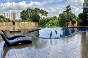 A swimming pool with lounge chairs, surrounded by a wooden deck and greenery. - Day Use Inn At Serpong Green View Apartment Bsd (South Tangerang)