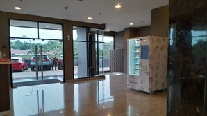 A modern hotel lobby with a glass entrance, a reception desk, and a patterned wall unit. - Day Use Inn At Serpong Green View Apartment Bsd (South Tangerang)