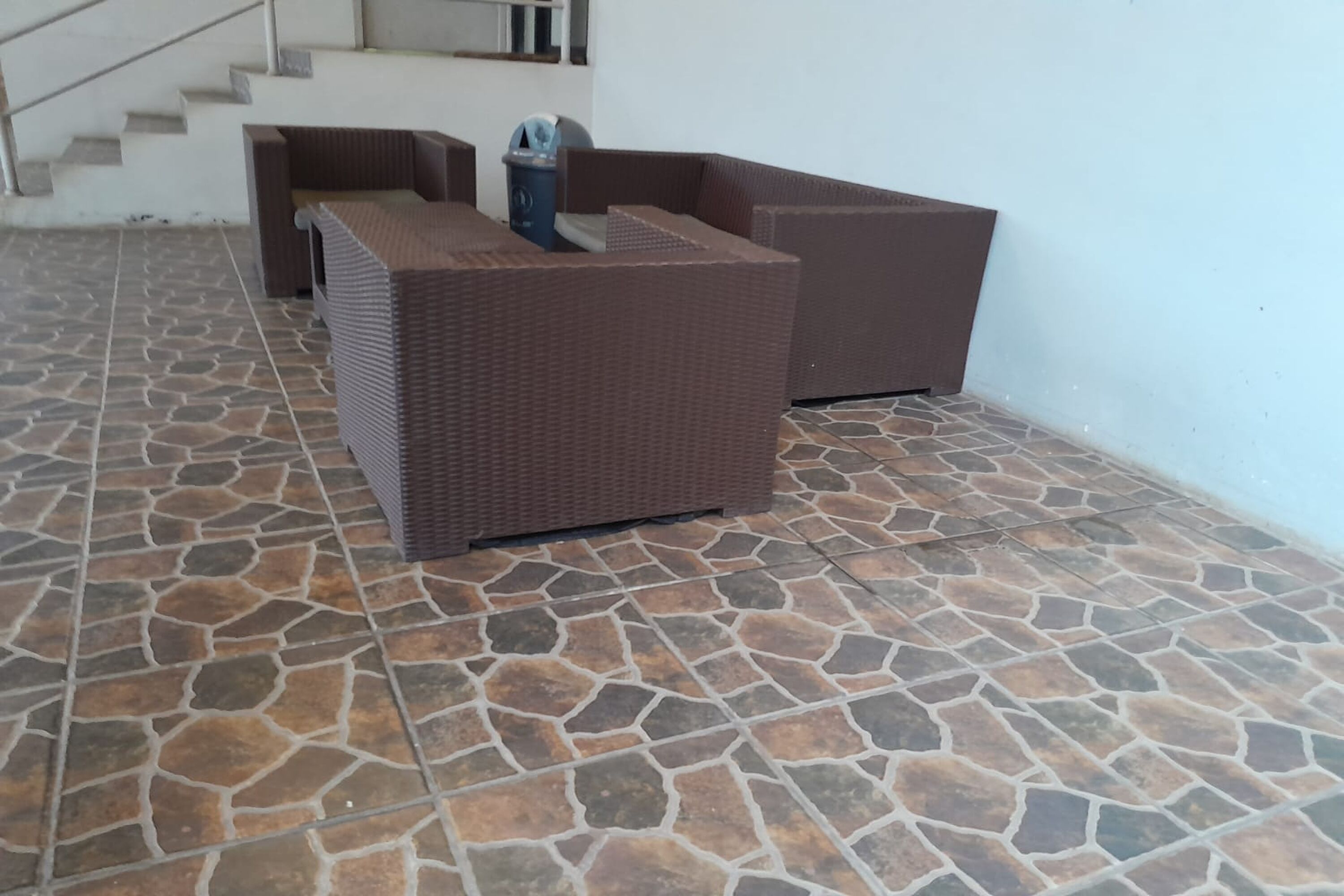 A room with a stone-tiled floor, a brown wicker sofa, and a trash bin.