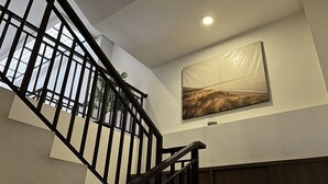 A staircase with black railings and a wooden handrail, leading to a room with a large window and a framed picture on the wall. - Good Day Inn (Jakarta)